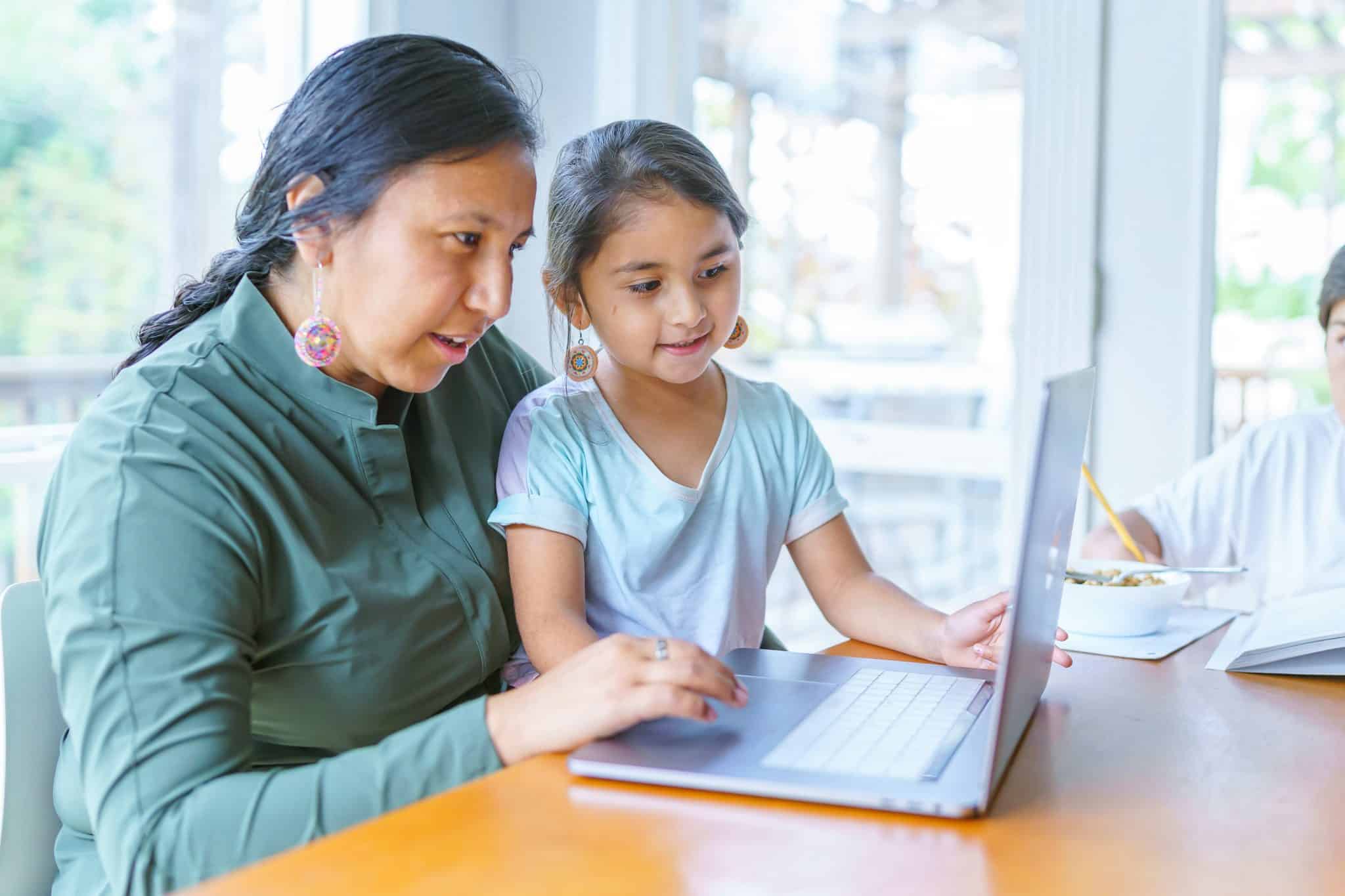 Woman looking up vaccine misinformation on her laptop with her daughter seated in her lap.