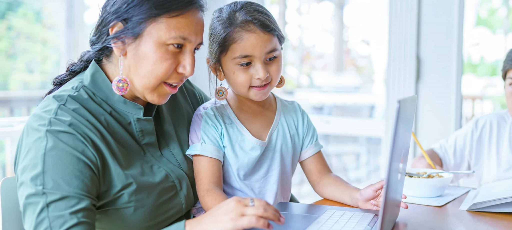 Woman looking up vaccine misinformation on her laptop with her daughter seated in her lap.